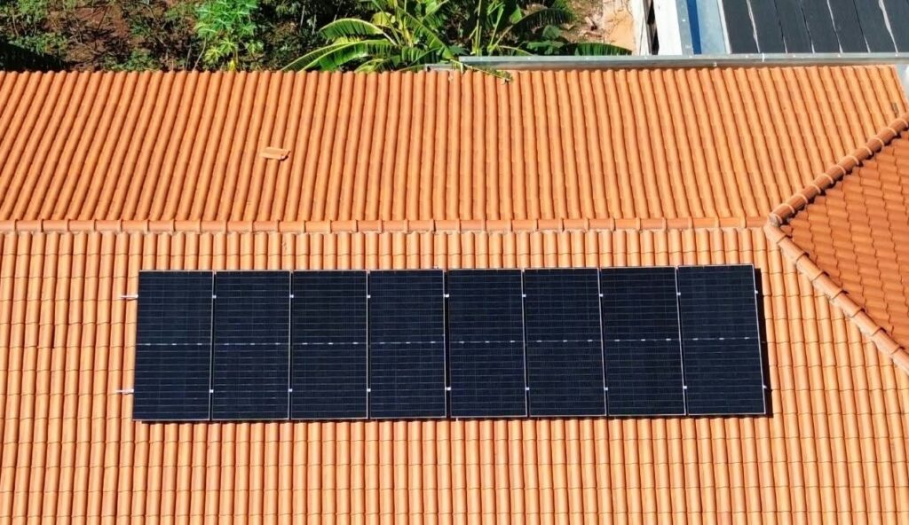 Vista aérea de oito painéis solares instalados em linha sobre um telhado de telhas cerâmicas