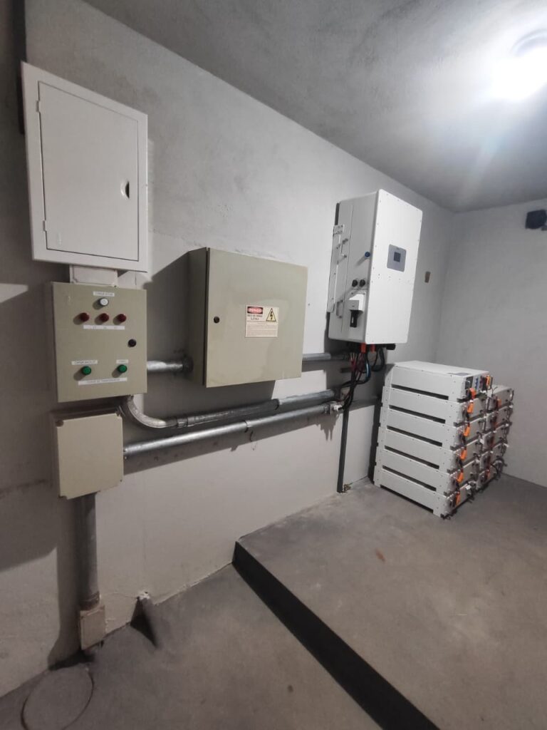 Sala técnica com inversor e quadros na parede e módulos de bateria Bos-W no piso