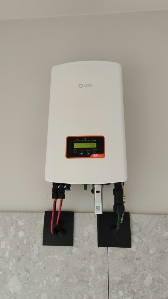 Inversor branco com visor instalado na parede, com cabos saindo pela parte de baixo